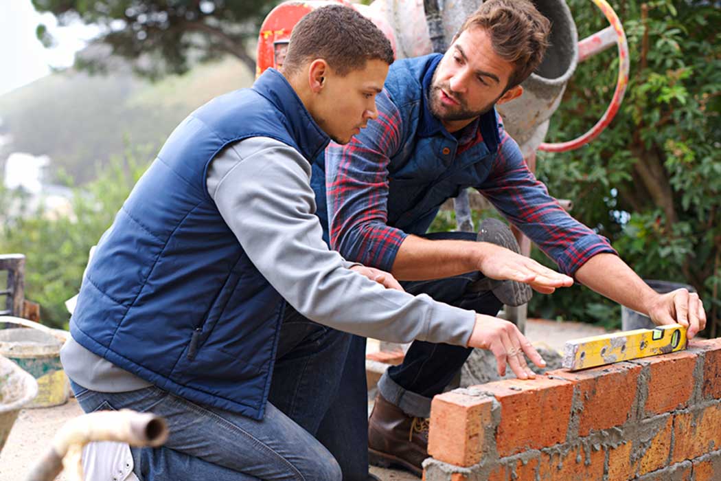 Bricklayer showing young person how to build a wall